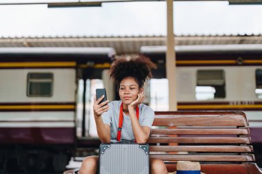 Asyalı Afro-Amerikan genç kız tren istasyonunda beklerken akıllı telefon mafyası kullanarak seyahat ediyor.
