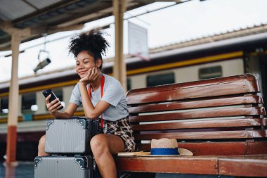 Asyalı Afro-Amerikan genç kız tren istasyonunda beklerken akıllı telefon mafyası kullanarak seyahat ediyor.