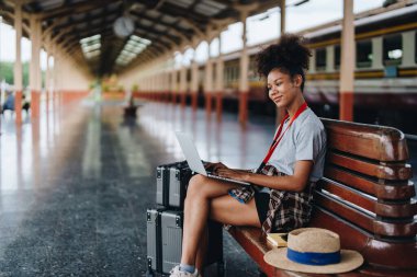 Asyalı Afro-Amerikan genç kız bir istasyonda tren beklerken bilgisayarla seyahat ediyor.