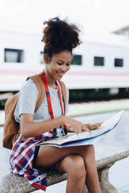Asyalı genç Afro-Amerikan bir gezgin günlük giysiler içinde elinde harita tutuyor ve doğru yolu arıyor. 