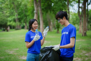 Çok ırklı gönüllüler, kamu parkındaki kirliliği azaltmak için geri dönüşüm için plastik atık toplamak amacıyla ellerinde siyah çöp torbaları tutarak zamanlarını bağışlıyorlar.