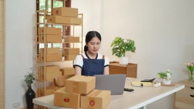 Küçük bir girişimin portresi ve KME sahibi, cep telefonu ve dizüstü bilgisayar kullanan Asyalı bir bayan girişimci, müşteriler için iç kutulara koymadan önce ürünleri organize etme siparişlerini kontrol ediyor. Yüksek