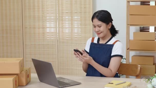 携帯電話やノートパソコンを使用しているアジアの女性起業家である小規模スタートアップと中小企業の所有者の肖像画は 顧客のためのインナーボックスにそれらを梱包する前に製品を整理するための注文をチェックします — ストック動画
