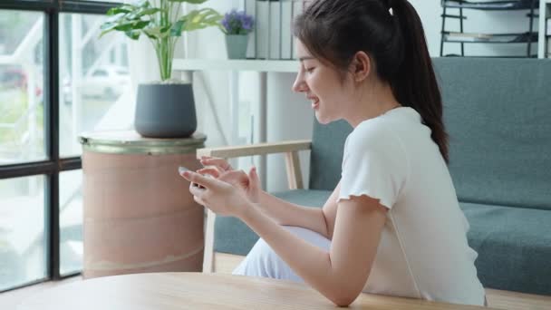 使用智能手机 浏览社交媒体 查看新闻 玩手机游戏或在沙发上发短信等方式放松了亚洲女性 千禧年女人在家里用手机技术 — 图库视频影像