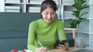 Sosyal medyada akıllı telefon sörfü yapan, haberleri kontrol eden, mobil oyunlar oynayan, mesajlaşan ve kanepede otururken hatırlamak için elinde kalem kalem tutan rahat Asyalı kadın. Yüksek kalite 4k