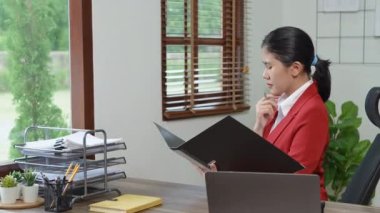 Düşünceli bir Asyalı iş kadınının portresi finansal tablolara bakıyor ve masasındaki bilgisayarı kullanarak pazarlama planları yapıyor. Yüksek kalite 4k görüntü