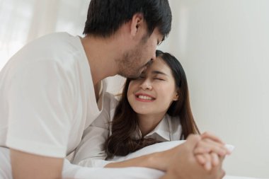 Yatakta yatan Asyalı romantik çift, şehvetli ön sevişmelerden zevk alıyor. Yatakta birlikte yatan genç ve şehvetli bir çift. Güzel bir çift yatakta öpüşüyor.