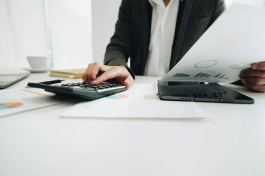 Ofisteki muhasebe belgesini kullanırken iş verilerini hesaplamak için hesap makinesi ve dizüstü bilgisayar üzerinde çalışan işadamı veya muhasebeci