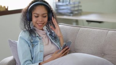 Kulaklık takan Asyalı hoş bir genç bayan dinlenirken koltukta oturup müzik dinlerken telefonu kullanmaya hazır. Yüksek kalite 4k görüntü