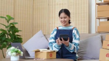Serbest çalışan Asyalı bir kadının işletme karını hesaplamak için dizüstü bilgisayar ve hesap makinesi kullanarak küçük bir iş kurması. Online pazarlama paketi öğeleri ve KME konseptiyle. Yüksek kalite