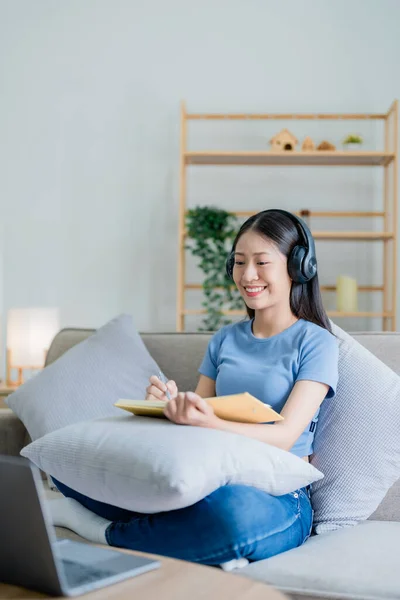 年轻的亚洲女人从耳机里听音乐 并在日记里为自己的工作想法写笔记 放松概念 — 图库照片