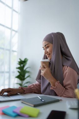 Laptop kullanan ve kahve içen Müslüman bir kadının portresi