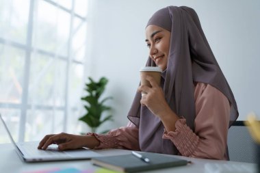 Laptop kullanan ve kahve içen Müslüman bir kadının portresi