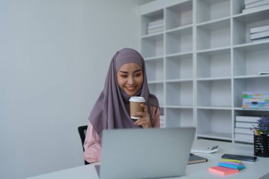 Laptop kullanan ve kahve içen Müslüman bir kadının portresi