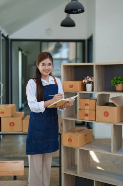 Bağımsız genç Asyalı kadın çevrimiçi satıcının küçük işletme girişimciliğine başlamak, bilgisayar kullanmak ve müşterilere dağıtım için ürünleri paketlemek için siparişler almaktır. KME dağıtım kavramı.