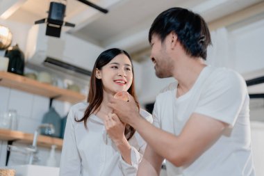 Gülümseyen eşiyle el ele tutuştuğu ve hafta sonları modern mutfakta yemek pişirmekten zevk aldığı mutlu genç bir erkek.