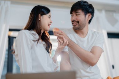 Gülümseyen eşiyle el ele tutuştuğu ve hafta sonları modern mutfakta yemek pişirmekten zevk aldığı mutlu genç bir erkek.