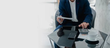 Ofisteki muhasebe belgesini kullanırken iş verilerini hesaplamak için hesap makinesi ve dizüstü bilgisayar üzerinde çalışan işadamı veya muhasebeci