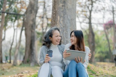 Yaşlanan bir annesi olan yetişkin bir kız çocuğu aşkı ifade ediyor ve parktaki ağacın altındaki tablet bilgisayara bakıyor.