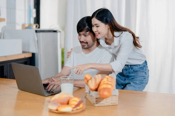 stock image Happy young loving family couple looking at laptop computer screen, reading ecipes. Wife showing embrace to husband to pretty joyful husband, sitting at table in kitchen at home in weekend