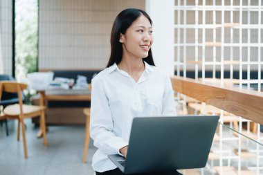 Bir kafede bilgisayar kullanırken gülümseyen bir yüz ve mutluluk gösteren Asyalı serbest çalışan genç bir kadın. Serbest meslek, serbest meslek, rahatlama.