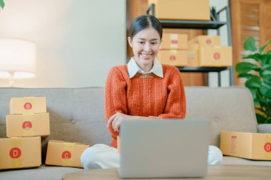 Bağımsız genç Asyalı kadın çevrimiçi satıcının küçük işletme girişimciliğine başlamak, bilgisayar kullanmak ve müşterilere dağıtım için ürünleri paketlemek için siparişler almaktır. KME dağıtım kavramı.