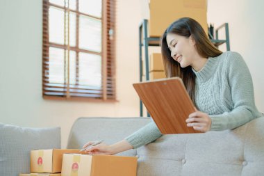 Bağımsız genç Asyalı kadın çevrimiçi satıcının küçük işletme girişimciliğine başlamak, bilgisayar kullanmak ve müşterilere dağıtım için ürünleri paketlemek için siparişler almaktır. KME dağıtım kavramı.