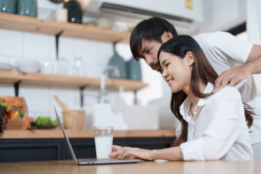 Mutlu yüzler gösteren genç evli bir çift ve evde dinlenirken ev gelirlerini ve giderlerini hesaplamak için bilgisayar ve defter kullanıyorlar.