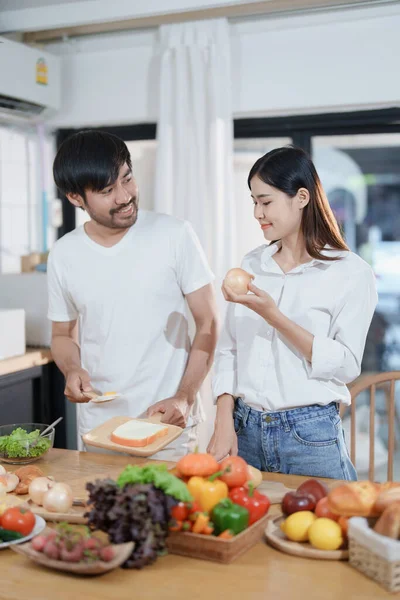 Smiling man hugging woman, two people standing and joyfully looking at each other. Young couple happily spending time in cozy modern kitchen at home