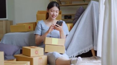 Bağımsız Asyalı kadın çevrimiçi satıcının küçük işletme girişimcisi olarak bir müşteriyle telefonda konuşuyor ve müşteriye teslimat için ürünleri paketliyor. ve KOBİ teslimat konsepti. Yüksek