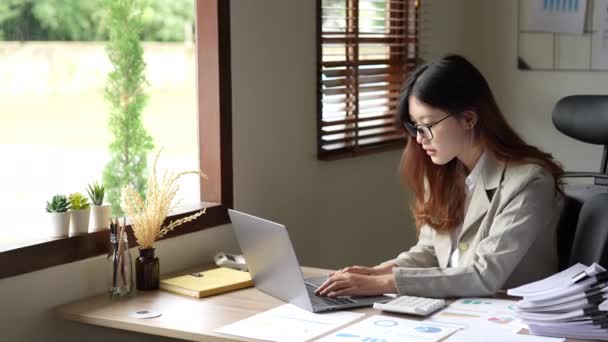 年轻的亚洲商人或簿记员在使用电脑和木制桌子上的文件编制财务预算时表现出快乐的姿态 高质量的4K镜头 — 图库视频影像