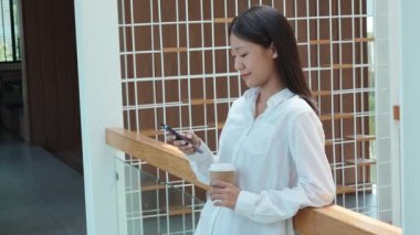 Genç Asyalı serbest meslek sahibi bir kadın gülümseyen bir yüz ve mutluluk gösterirken akıllı telefon ile iş konuşuyor ve bir kafede kahve içiyor. Yüksek kalite 4k görüntü