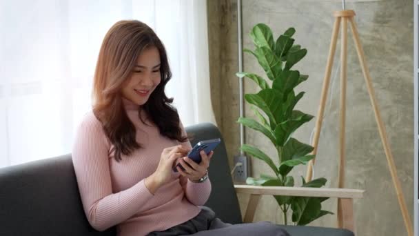 迷人的美丽的亚洲女人坐在沙发上 用智能手机放松自己 高质量的4K镜头 — 图库视频影像