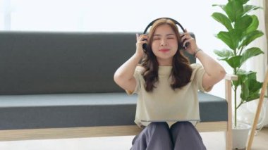 Çekici, güzel, Asyalı bir kadın evde kanepede otururken müzik dinlemek için tablet ve kulaklık kullanıyor. Yüksek kalite 4k görüntü
