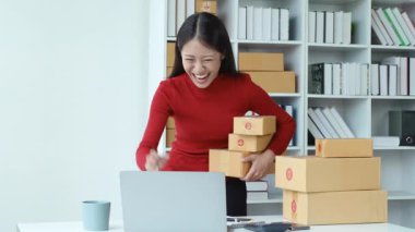 E-ticaret, küçük işletme, sme, teslimat kutusunu tutan güzel Asyalı kadın ve müşterilerin siparişi satın aldığını görünce sevinen bilgisayara bakıyor. Yüksek kalite 4k görüntü