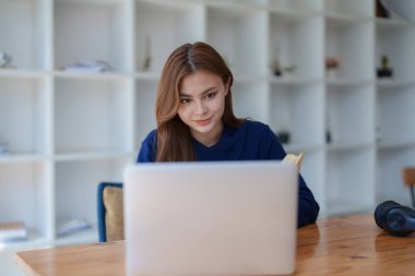 Mutlu Latin kız kolej öğrencisi uzaktan öğrenim kursu, uzak üniversite web sitesi ya da laptop üzerinden konuşma videosu alıyor ve evdeki ya da kampüsteki sanal toplantı seminerinde not defteri kullanıyor.