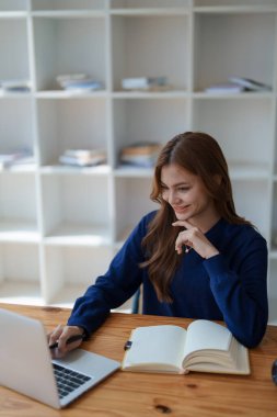 Mutlu Latin kız kolej öğrencisi uzaktan öğrenim kursu, uzak üniversite web sitesi ya da laptop üzerinden konuşma videosu alıyor ve evdeki ya da kampüsteki sanal toplantı seminerinde not defteri kullanıyor.