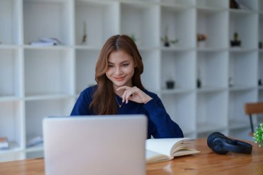 Mutlu Latin kız kolej öğrencisi uzaktan öğrenim kursu, uzak üniversite web sitesi ya da laptop üzerinden konuşma videosu alıyor ve evdeki ya da kampüsteki sanal toplantı seminerinde not defteri kullanıyor.