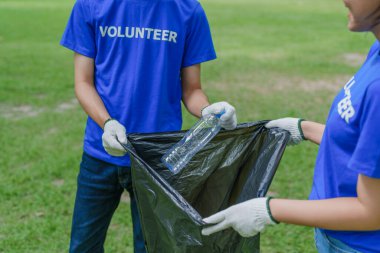 Çok ırklı gönüllüler, kamu parkındaki kirliliği azaltmak için geri dönüşüm için plastik atık toplamak amacıyla ellerinde siyah çöp torbaları tutarak zamanlarını bağışlıyorlar.