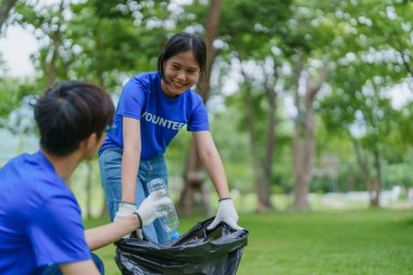 Çok ırklı gönüllüler, kamu parkındaki kirliliği azaltmak için geri dönüşüm için plastik atık toplamak amacıyla ellerinde siyah çöp torbaları tutarak zamanlarını bağışlıyorlar.