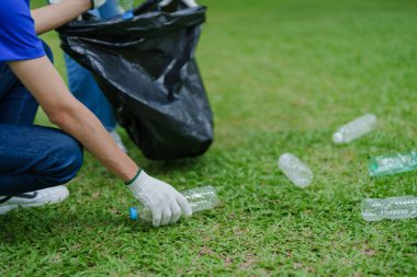 Çok ırklı gönüllüler, kamu parkındaki kirliliği azaltmak için geri dönüşüm için plastik atık toplamak amacıyla ellerinde siyah çöp torbaları tutarak zamanlarını bağışlıyorlar.