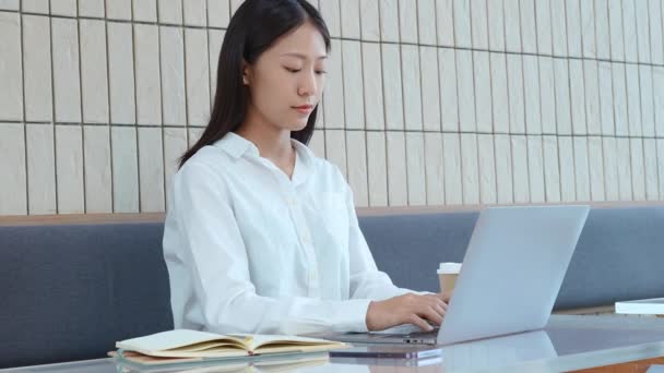 若いアジアの女性がパソコンを操作し ペンを持ってカフェのノートブックにメモを取ります 高品質4K映像 — ストック動画