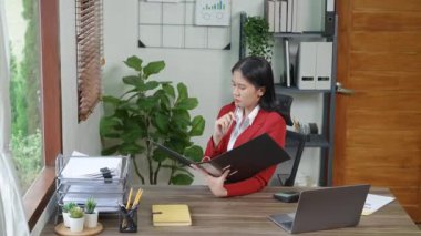Düşünceli bir Asyalı iş kadınının portresi finansal tablolara bakıyor ve masasındaki bilgisayarı kullanarak pazarlama planları yapıyor. Yüksek kalite 4k görüntü
