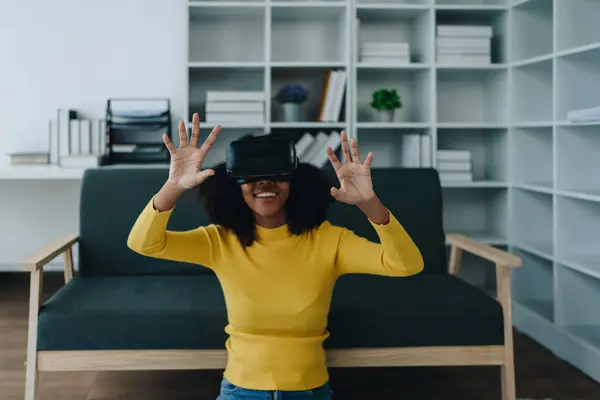 Positive African American woman teenager in futuristic VR helmet laughing and relaxing. Youthful girl is delighted with high-tech video games and virtual reality gadgets sits, Artificial Intelligence.