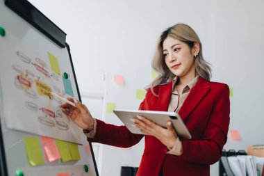 Düşünceli bir Asyalı iş kadınının portresi finansal tablolara bakıyor ve masasındaki bilgisayarı kullanarak pazarlama planları yapıyor..