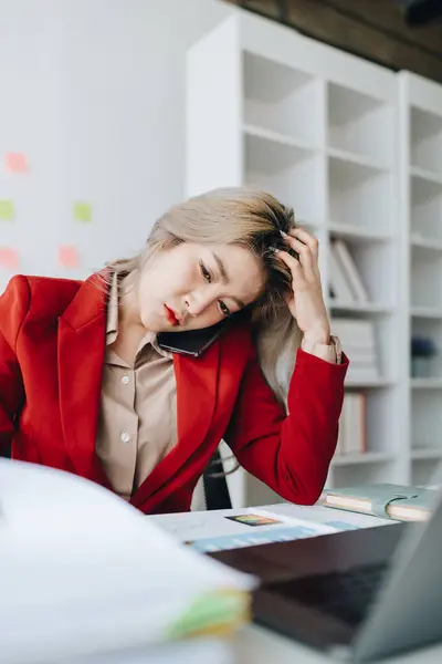 Busy businesswoman wearing a suit busy with work workaholic while sitting at work clear paperworks with documents and talk on the phone on your smartphone hear the hustle and bustle, busy concepts