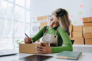 Bağımsız Asyalı kadın çevrimiçi satıcının küçük işletme girişimcisi olarak bir müşteriyle telefonda konuşuyor ve müşteriye teslimat için ürünleri paketliyor. ve KME dağıtım kavramı.