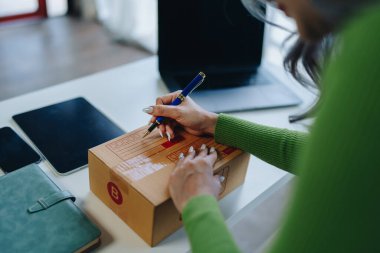 Bağımsız Asyalı kadın çevrimiçi satıcının müşterilere ve KOBİ dağıtım konseptine göndermek üzere ürünlerini paketleyen küçük işletme girişimcisi başlatılıyor.