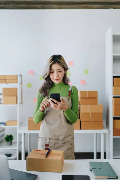 Starting small business entrepreneur of independent Asian female online seller talking on the phone with a customer and packing products for delivery to the customer. and SME delivery concept.