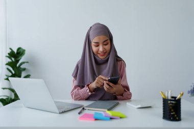 Müslüman kadın çalışan. Ofisteki müşterilerle konuşmak için telefonu kullanıyor.